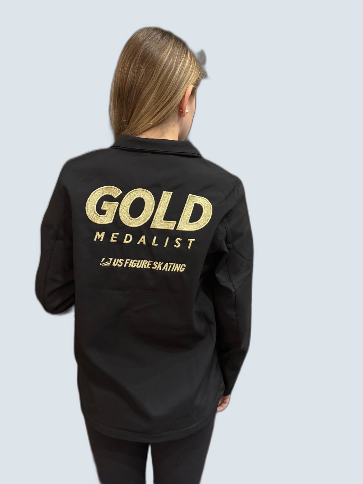 Skater wearing a black US Figure Skating Gold Medalist jacket, photographed from behind